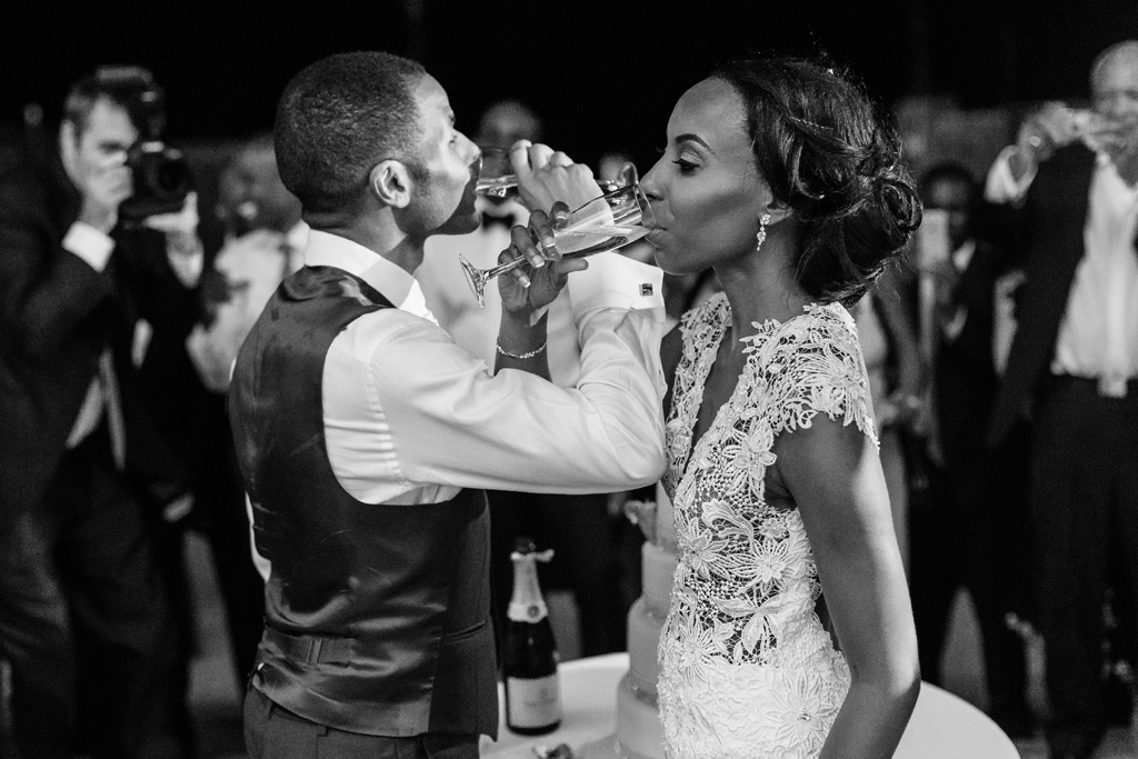 Fotografo Matrimonio Villa Erba I due sposi, Tony e Ayesha, bevono champagne con le braccia intrecciate