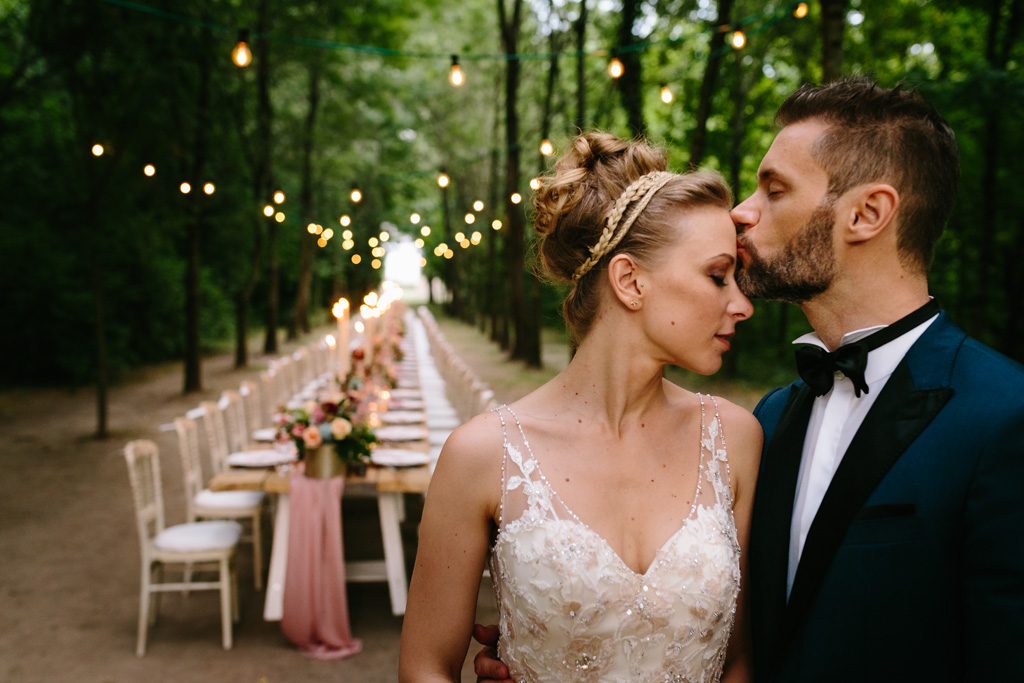 Fotografo Matrimonio Convento Dell'Annunciata Medole Lo sposo bacia la sposa sulla fronte davanti al tavolo per la cena di nozze