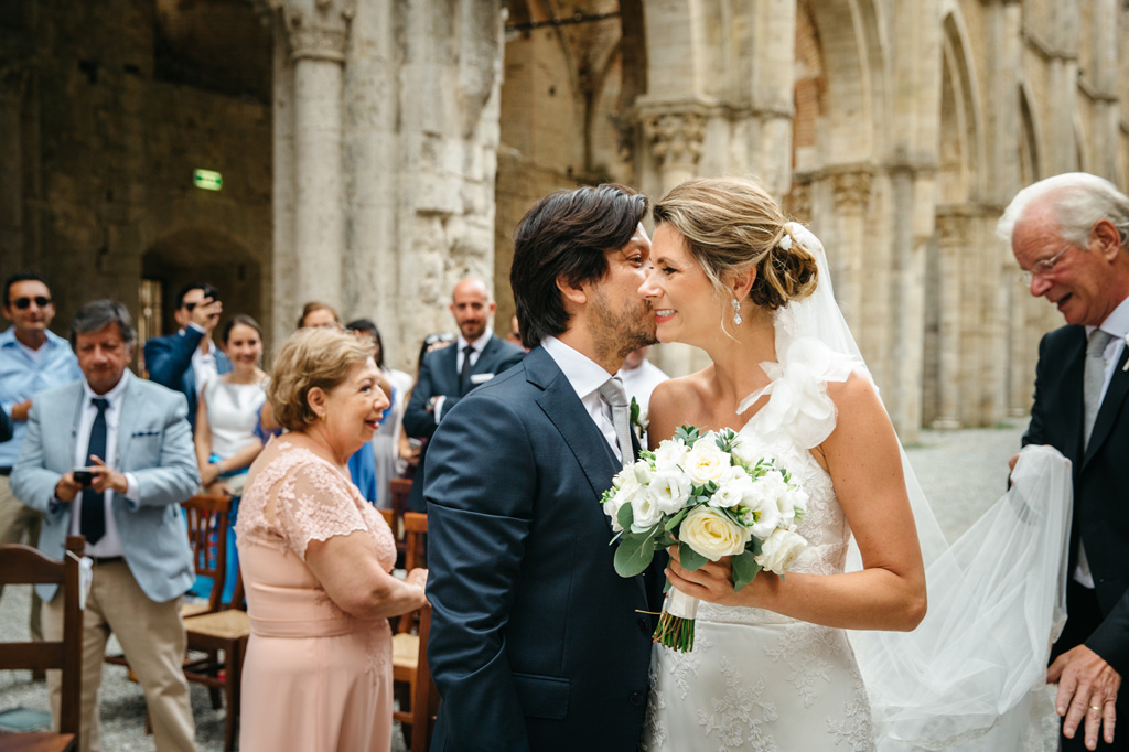 Fotografo Matrimonio Basilica San Galgano Toscana Lo sposo bacia la sposa sulla guancia mentre il padre le sistema il velo