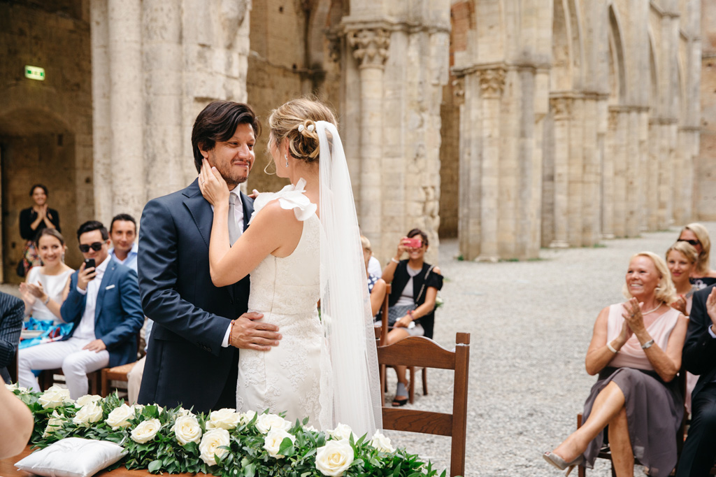 Fotografo Matrimonio Basilica San Galgano Toscana Gli sposi felici si tengono vicini mentre gli invitati applaudono