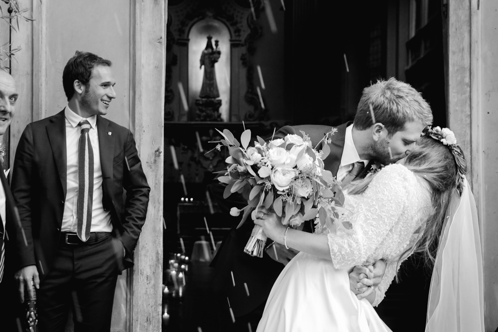 Wedding Photographer Como Lake Lo sposo bacia la sposa fuori dalla chiesa sotto una cascata di riso portafortuna