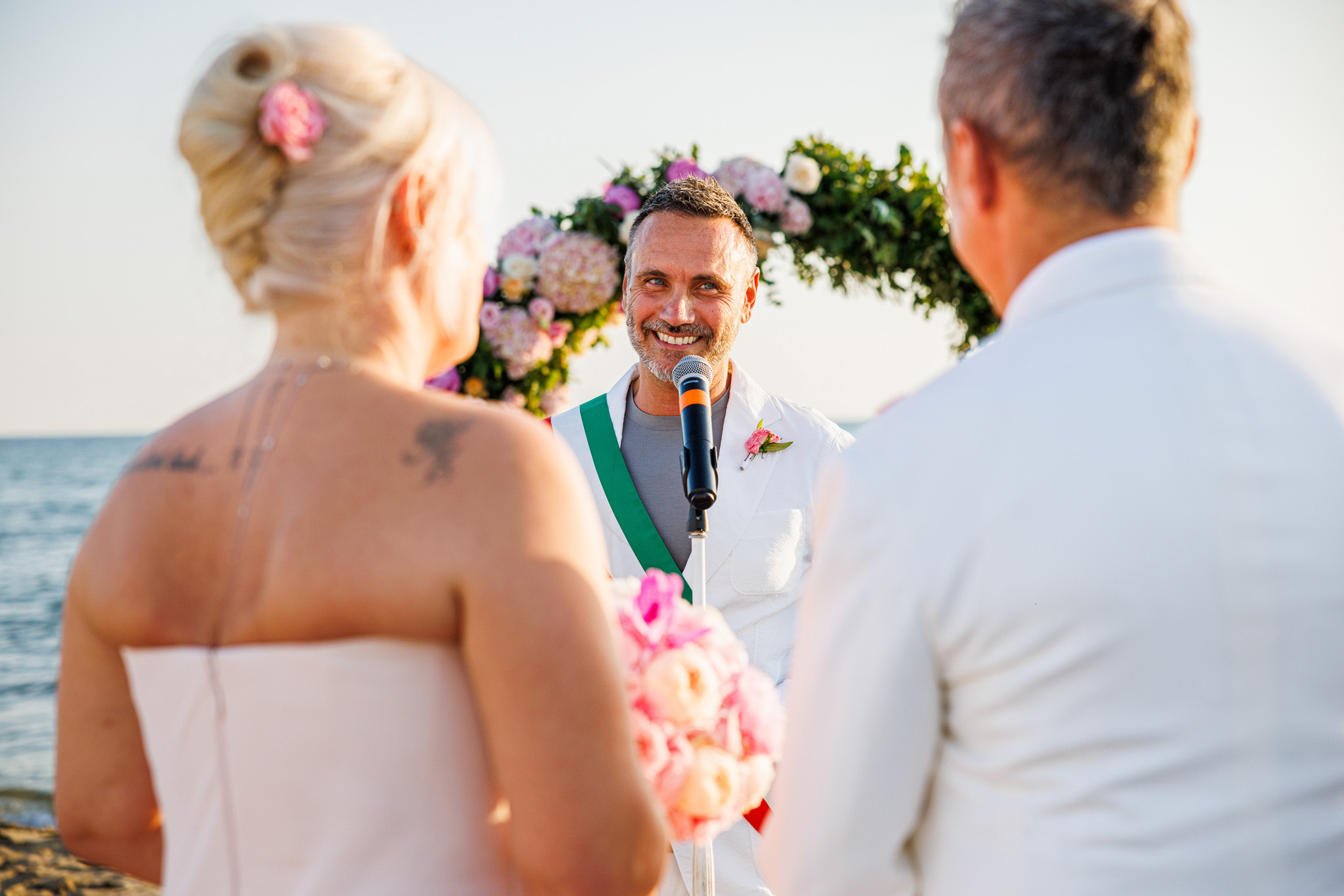 Destination Wedding Tuscany Un cerimoniere con gli sposi il giorno del loro matrimonio, durante la cerimonia sulla spiaggia