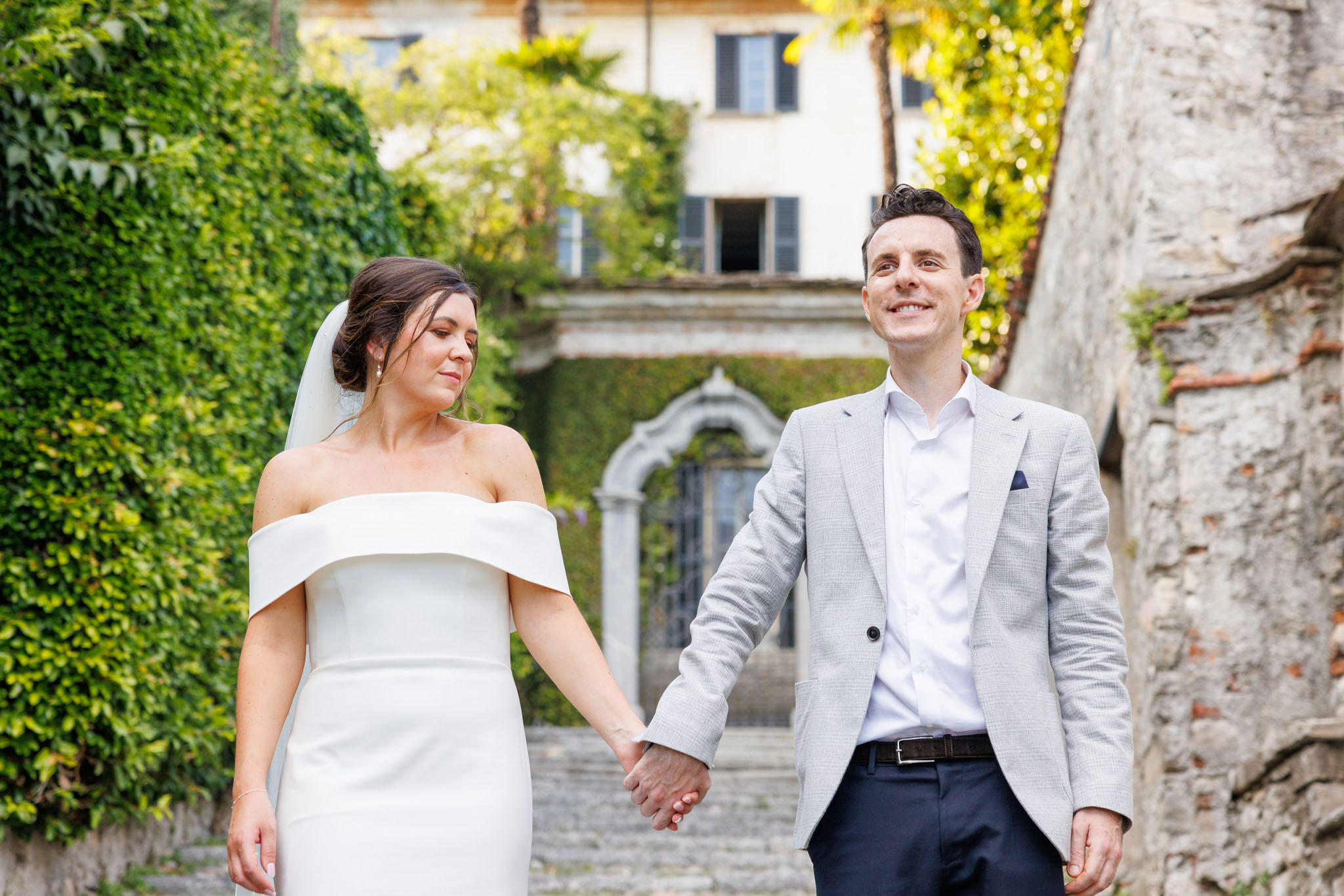 Destination Wedding Photographer Como Uno sposo e una sposa che si tengono per mano alle porte di una villa sul lago di Como